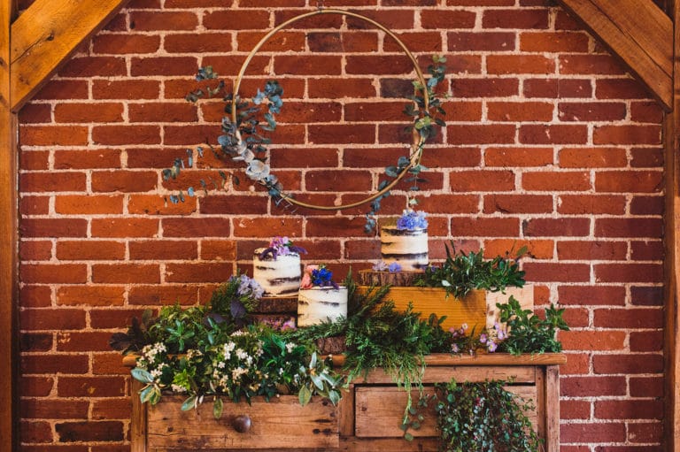 A beautiful deconstructed three tier wedding cake, surrounded by foliage decoration