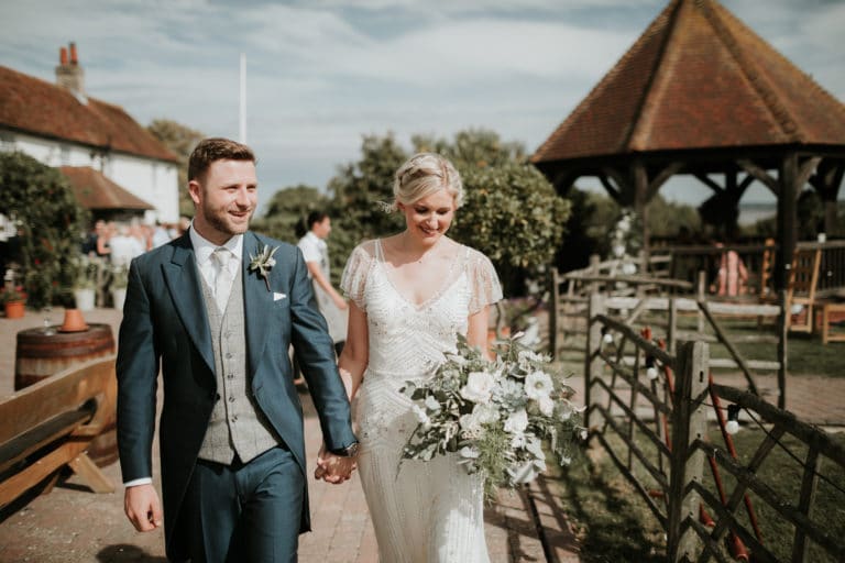 A bride and groom walking hand in hand towards the secret orchard at barn wedding venue, The Ferry House.