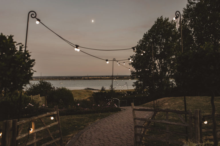 The Ferry House wedding garden at twilight, with gleaming festoon lights and the estuary beyond