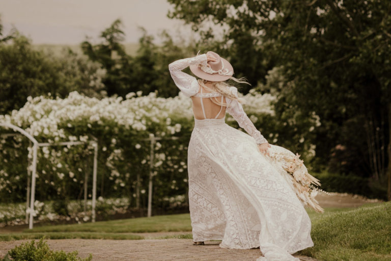 A boho bride walking towards the rose arch at Kent barn wedding venue, The Ferry House.