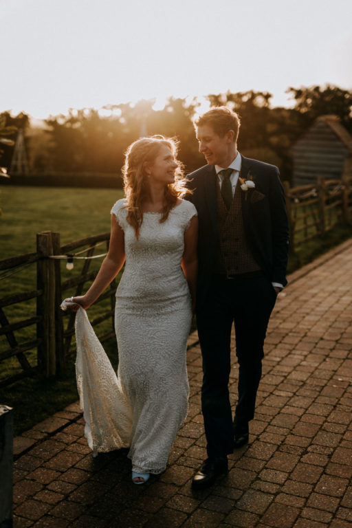 A bride and groom taking a stroll through the wedding gardens at The Ferry House with the sunset in the background.