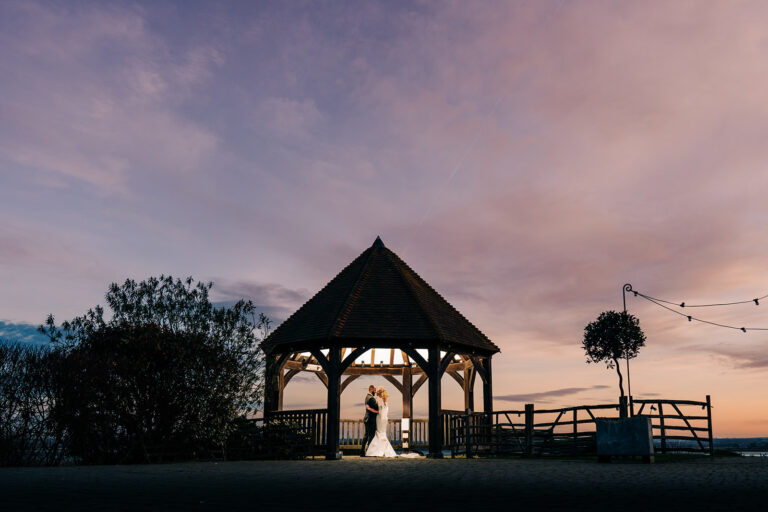 A wedding couple standing underneath an illuminated Oak Gazebo at twilight