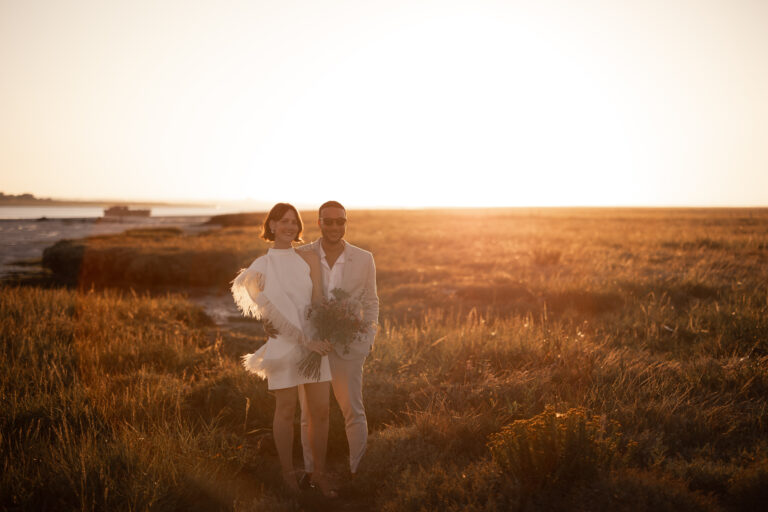 A cool wedding couple standing among golden wild meadows at sunset