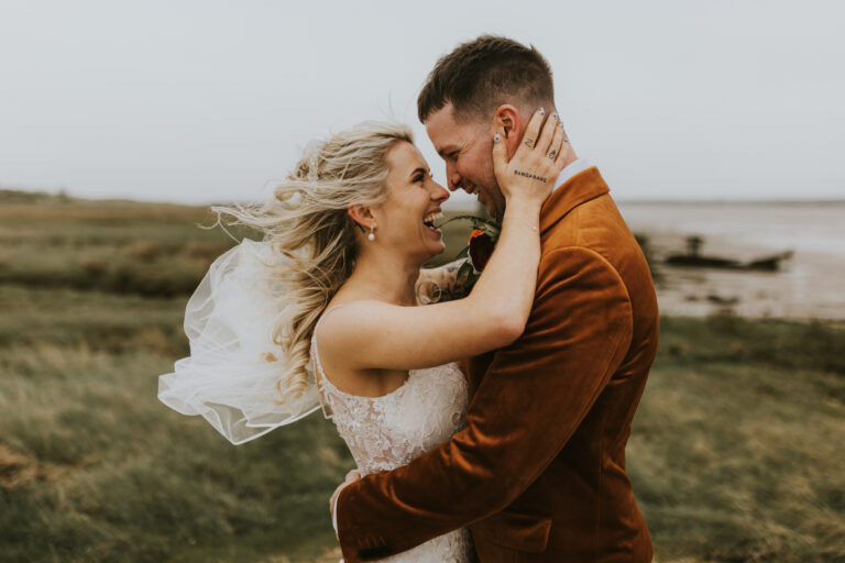 A smiling couple on their wedding day beside the Swale estuary at The Ferry House in Kent