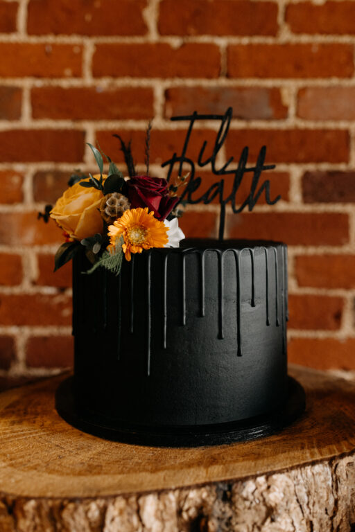 A black wedding cake with 'til death' topper at the Kent wedding venue, The Ferry House.