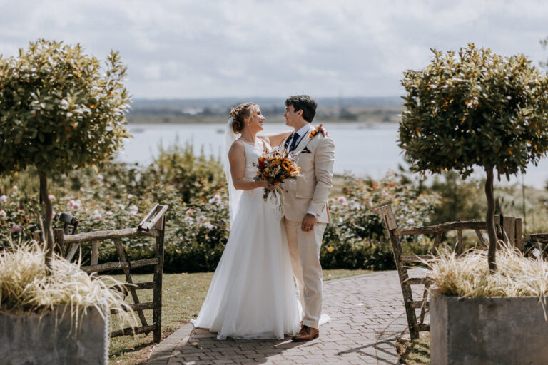 A couple in the landscaped gardens of The Ferry House wedding venue in Kent, with the Swale estuary in the background.