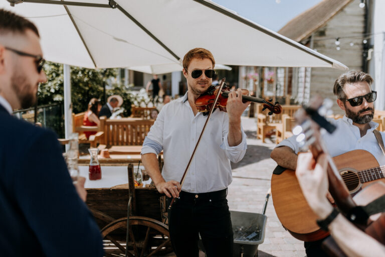 Musicians playing outdoors during a sunny wedding drinks reception