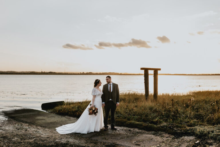 A couple married at The Ferry House wedding venue, standing beside the Swale estuary in Kent at sunset.