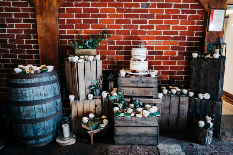 A stunning wedding cake and cupcake display on apple crates, in a rustic wedding barn