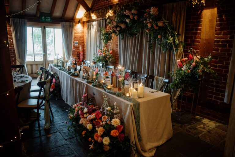 A wedding reception top table with colourful flowers, set in a wedding barn venue